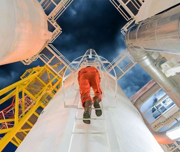 Operario ascendiendo por una escalera vertical en una planta industrial bajo un cielo de tormenta